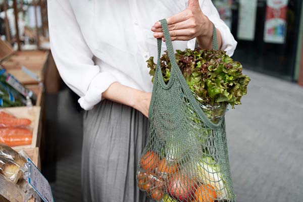 Woman carrying groceries in reusable tote bag, reducing plastic waste