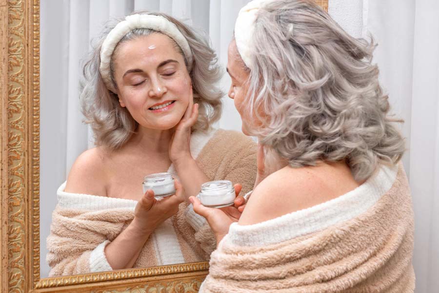 Elderly woman applying skincare, highlighting self-care and aging gracefully.