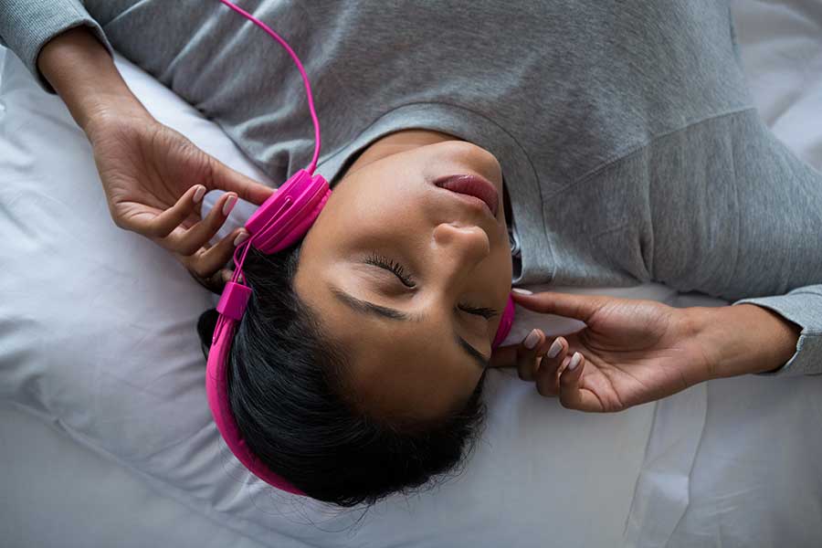 Woman lying down, listening to sound healing frequency with headphones.