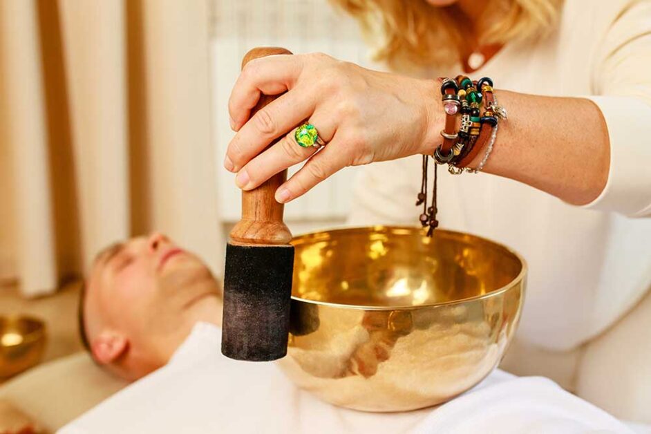 Practitioner using a Tibetan singing bowl for sound healing therapy.