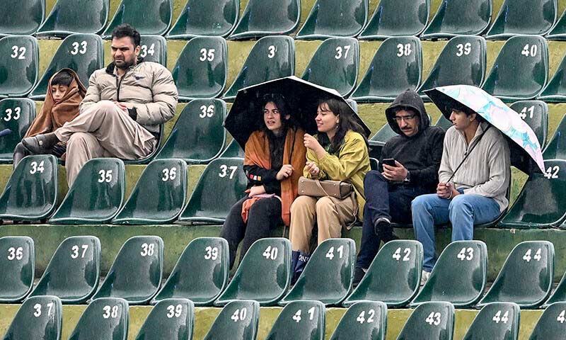 Spectators sitting under umbrellas as rain disrupts play