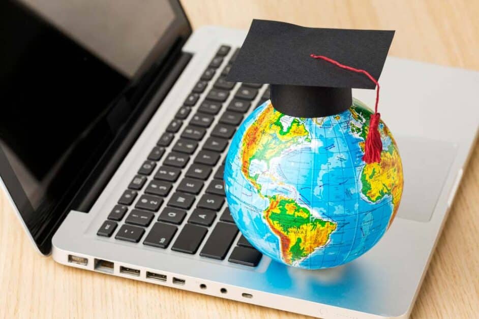 Small globe with a graduation cap placed on a laptop keyboard, symbolizing digital learning and global education trends.