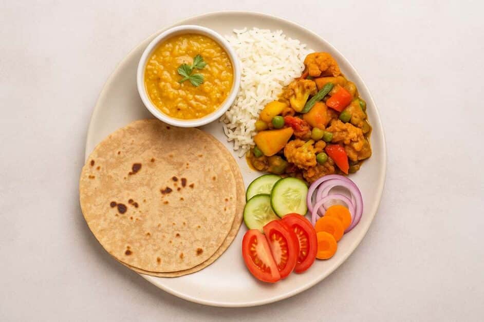 Healthy Indian diet plate with chapati, rice, dal, cooked vegetables, and fresh salad