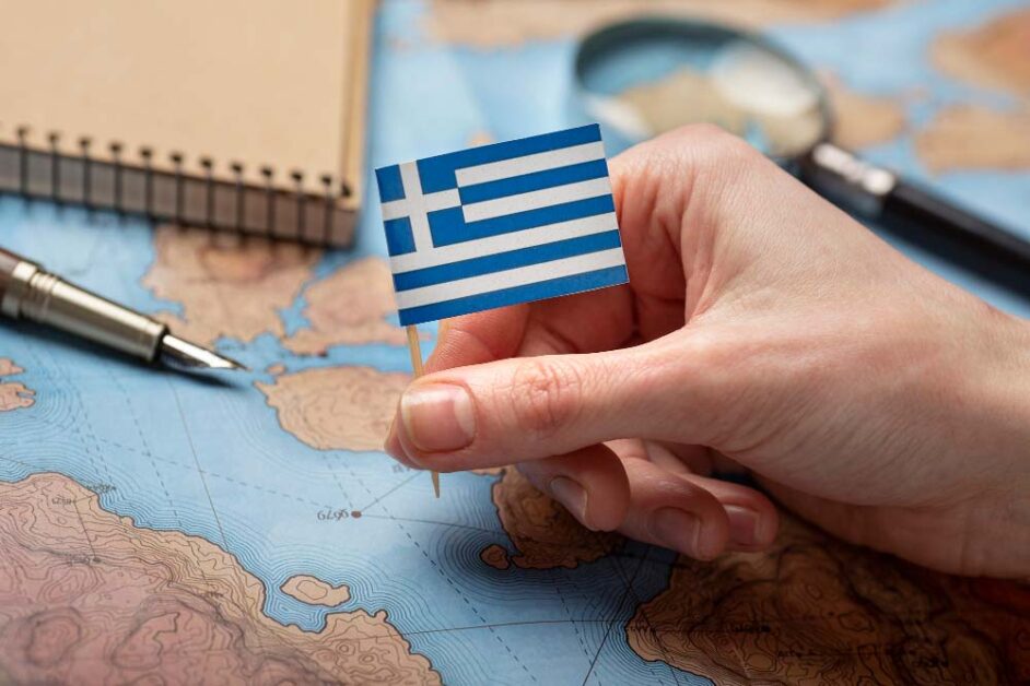 Hand holding Greek flag over map symbolizing work migration.