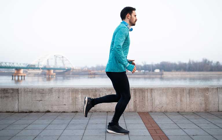 Man running near riverside bridge illustrating high-intensity exercise compared to Japanese Interval Walking.