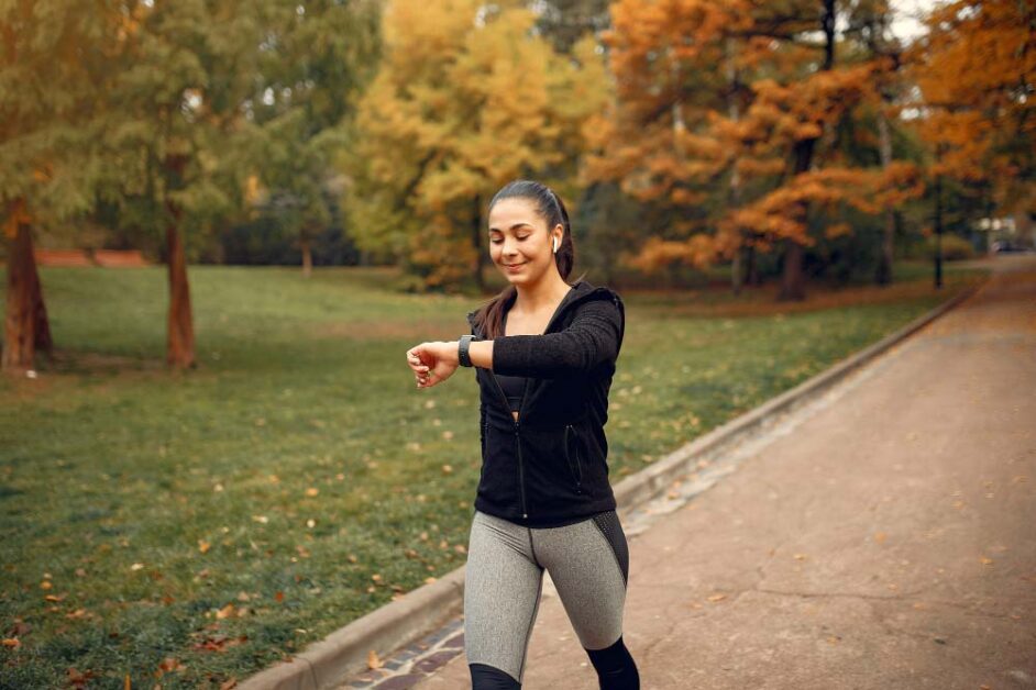 Woman checking her smartwatch while walking outdoors to track interval walking timing.